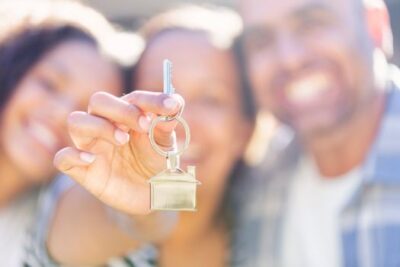 Smiling family holding a house key in front of their new home