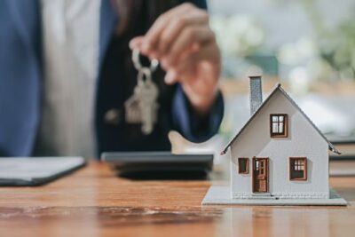 Close-up of a miniature house model on a table with a man holding a key in the background