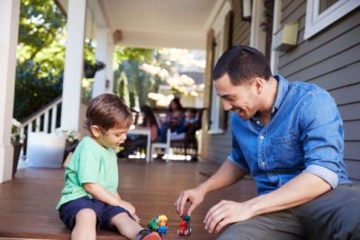 Father playing with young son on front porch of family home