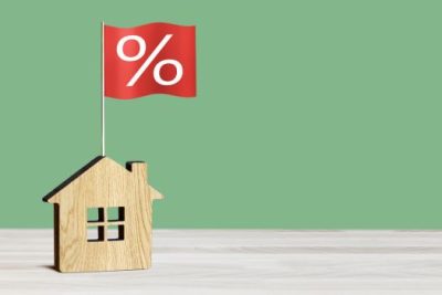 Wooden house model with red percentage flag symbolizing changing mortgage rates