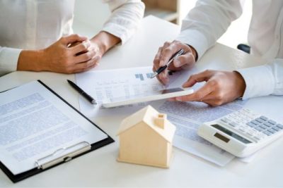 Homebuyer reviewing mortgage documents with a loan officer, financial charts, and calculator on the table