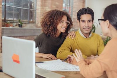 Smiling couple meeting with mortgage advisor reviewing home loan documents in a modern office