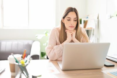 Young woman researching mortgage credit score requirements on a laptop at home office