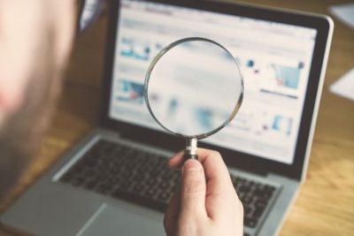 Person using magnifying glass to analyze online home-buying search results on a laptop