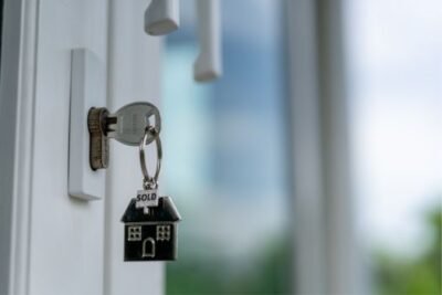 House-shaped keychain labeled “sold” hanging from a key in a new home door, symbolizing home purchases and buyer demand.