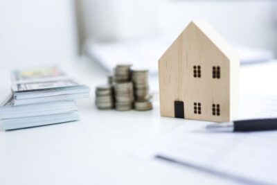Stacks of cash, coins, and a small wooden house model representing mortgage rates and housing affordability trends.